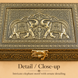 Detailed close-up of the handcrafted Elephant Design Brass Decorative Storage Box highlighting the raised double elephant artwork, intricate floral engraving, textured antique gold surface, ornamental border patterns and traditional metal clasp craftsmanship.