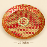 Top-down view of a large 20-inch circular brass serving thali tray featuring red and gold enamel floral art with a central motif. Placed against a clean beige backdrop with brown text reading '20 Inches' centered beneath.