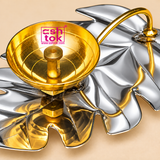 Detailed close-up view of a Leaf Design Brass Puja Diya highlighting its beautifully polished golden brass oil lamp bowl, centrally positioned cylindrical wick holder, decorative curved golden stem, and reflective silver-finish leaf-shaped tray. The brass bowl features a smooth circular rim, bright golden interior, finely defined concentric circular patterns, and a small raised central holder with a circular opening for positioning a cotton wick. The polished golden metallic surface displays warm reflection