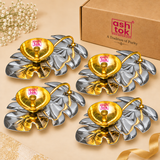 Four decorative Leaf Design Brass Puja Diyas arranged together in an elegant bulk gifting presentation on a premium beige studio background, featuring matching polished golden brass oil lamp bowls mounted on reflective silver-coloured leaf-shaped bases. Each diya features a circular golden bowl with finely detailed concentric interior rings, a centrally positioned cylindrical wick holder, and a gracefully curved golden metallic stem extending towards the opposite end of the decorative leaf tray. The silver 