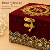 Extreme close-up macro photograph highlighting the rich plush texture of the deep red maroon velvet, the intricate gold thread floral mandap embroidery on the top lid, the detailed vintage brass latch clasp secured with screws, and the raised 3D metallic scroll pattern along the antique gold base of the decorative jewellery box.