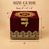 Comprehensive size guide diagram for a square royal maroon velvet jewellery gift box showing exact dimensions of 4 inches in width, 4 inches in height, and 4 inches in depth with dimensional arrows on a neutral beige background. The box features an ornate gold mandala-style embroidered pattern on the top lid, a vintage brass metal flip-latch clasp on the front center, and a heavy antique gold metallic carved decorative border around the bottom base.