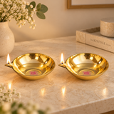 Set of 2 Matt Finish Brass Pankti Diyas styled in a warm modern home setting with soft decor and gentle flames, showing their use as elegant festive and decorative oil lamps. The brass diyas feature shallow oil bowls and pointed spouts, suitable for table styling, festive decor and traditional lighting.