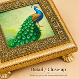Close-up detail image of Meenakari Design Chowki Peacock focusing on the intricate floral metalwork border, rich gold-toned texture, decorative raised legs, and the colorful central peacock design, showcasing the craftsmanship and ornamental detailing of the chowki.