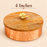Size guide image of a traditional copper-coloured metal dry fruit bowl featuring a round hammered body and removable natural wooden lid with a decorative golden leaf-shaped knob. The container measures approximately 4 inches in diameter and 3 inches in height. Measurement arrows highlight the compact circular dimensions and height of the lidded storage bowl, helping customers understand its size for dry fruit storage, sweet presentation, festive gifting and decorative household use.