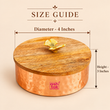 Size guide image of a traditional copper-coloured metal dry fruit bowl featuring a round hammered body and removable natural wooden lid with a decorative golden leaf-shaped knob. The container measures approximately 4 inches in diameter and 3 inches in height. Measurement arrows highlight the compact circular dimensions and height of the lidded storage bowl, helping customers understand its size for dry fruit storage, sweet presentation, festive gifting and decorative household use.