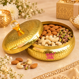 Metal dryfruit gift box shown in a festive lifestyle setting with the lid partially open and filled with almonds, cashews and pistachios, styled with soft floral decor and warm gifting elements to show its use for serving dry fruits, festive gifting and home decor.