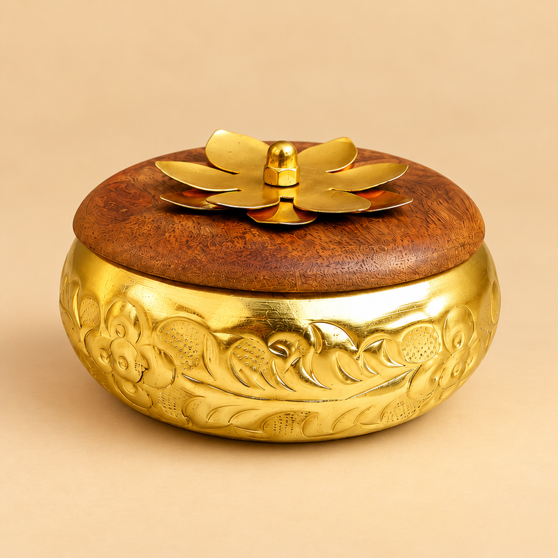 Brass-coloured metal gift box with engraved floral body and wooden lid with metal flower handle, shown closed on a beige background.