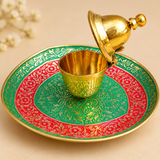 Close view of a golden meenakari kumkum box placed at the center of a red and green decorative plate on a beige background