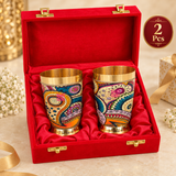 Set of 2 printed brass glasses presented in an elegant red gift box with soft inner lining, designed for premium gifting and special occasions. The brass tumblers feature a polished golden finish and colorful decorative printed pattern, making the set suitable for return gifts, festive gifting, wedding gifting, anniversaries, housewarming presents and celebration hampers.