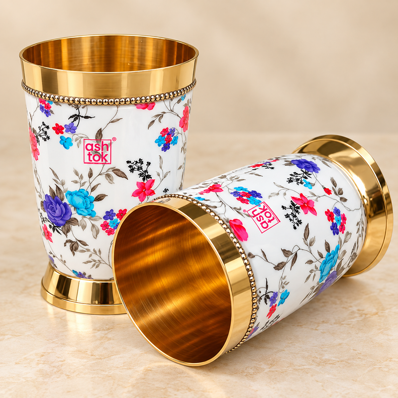 Printed brass water glasses with colorful floral design, polished golden interior, decorative gold rim and sturdy base, presented as a matching pair on a premium beige studio background for elegant drink serving and special occasions.