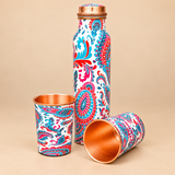Printed copper bottle with removed cap and 2 matching glasses on beige background