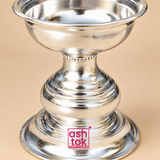 Detailed close-up view of a traditional silver finish Puja Deepam highlighting the polished upper bowl rim, reflective metal surface, decorative beaded neck detailing, smooth curved stem, concentric ring patterns, rounded central body and layered pedestal base, photographed against a soft beige studio background to showcase the craftsmanship, finish and traditional decorative styling of the deepam.