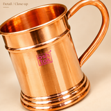 Detailed close-up of pure copper mug highlighting the smooth polished interior, rolled rim, sturdy curved handle, reflective copper surface and decorative stepped base, showing the craftsmanship and premium finish of the mug.