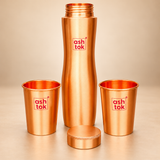 Pure copper water bottle displayed with its screw cap removed and placed in front, alongside two matching copper drinking glasses. The image highlights the bottle's threaded opening, smooth copper interior, brushed metallic exterior and coordinating drinking glasses on a beige studio background.