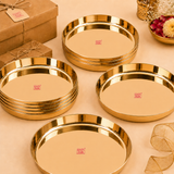 Stacked and displayed shiny round brass puja thalis displayed alongside brown kraft gift boxes tied with twine.