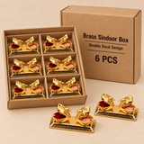 Six-piece set of Brass Sindoor Box Double Duck Design packed in a plain brown cardboard tray with simple divider sections and a matching corrugated outer box, with two complete pieces displayed outside the package to highlight the golden double-duck shape, decorative rectangular base, polished brass finish and traditional sindoor storage design, shown on a warm beige background as a practical non-premium packaging option for return gifts, festive gifting, wedding functions, religious ceremonies, retail pack