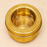 Top-angle view of a round brass storage box featuring a wide golden brass lid rim and transparent circular viewing window that reveals the empty interior of the container. The traditional cylindrical storage box has a smooth brass finish, clean circular design and removable lid, suitable for organizing dry spices, kitchen ingredients and small household items.