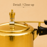 Close-up view of the top lid, brass pressure regulator whistle mechanism, and safety valve on an Ashtok brass pressure cooker.