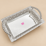 Silver rectangular serving tray displayed from a three-quarter side angle on a warm beige studio background, highlighting the depth of the tray, polished reflective base, detailed floral-style filigree side panels, decorative edge pattern, curved beaded handles and elevated feet, photographed with soft lighting to showcase the craftsmanship, structure and elegant silver finish for serving sweets, dry fruits, snacks, festive items and traditional gifting.
