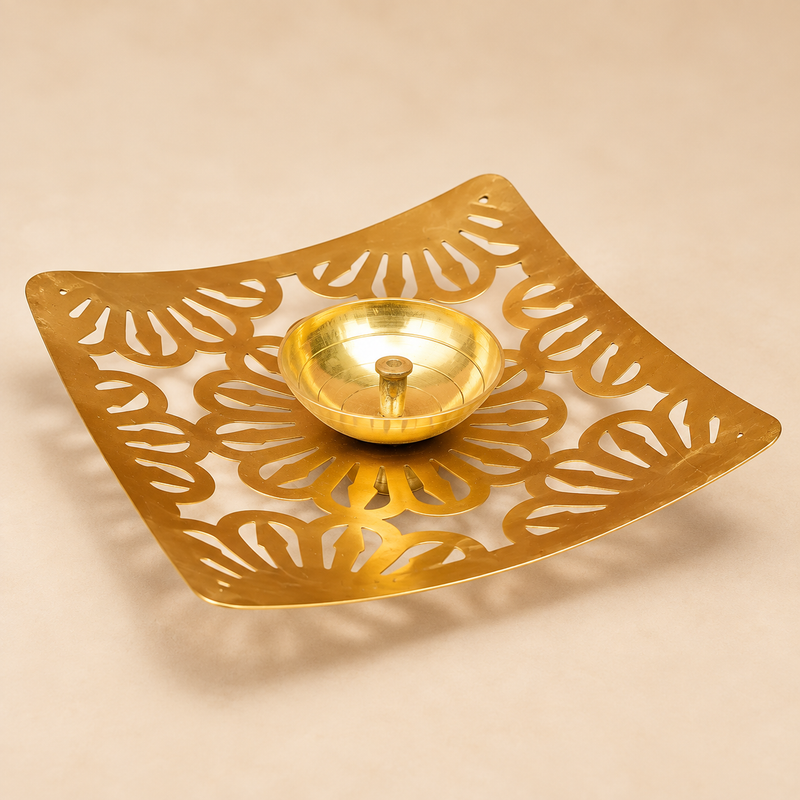 Square Shape Brass Jali Patta Diya with a warm polished brass finish, gently curved upturned square corners, intricate floral and leaf-inspired jali cutwork across the plate, and a centered round brass oil bowl with a sturdy wick holder, photographed as a clean three-quarter product image on a premium beige studio background with soft realistic shadows, suitable for daily puja, festive decor, home mandir use, Diwali lighting, traditional ceremonies and decorative gifting.