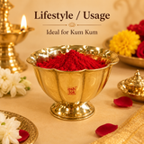 Traditional Indian pooja setup featuring a brass flower-shaped bowl filled with bright red kumkum powder, surrounded by a lit brass diya oil lamp, fresh white marigolds, red rose petals, and decorative brass pooja accessories.