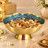 Turkish style brass Meenakari bowl shown in an elegant festive lifestyle setting filled with assorted dry fruits including almonds, cashews, pistachios and raisins. The decorative bowl features a scalloped rim, golden polished brass outer body, raised pedestal base and richly patterned blue and turquoise Meenakari interior with traditional floral and leafy motifs.