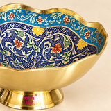 Detailed close-up view of a Turkish style brass Meenakari bowl focusing on the intricate multicolor artwork, scalloped golden rim and polished brass construction. The close framing shows the deep blue patterned interior, turquoise border, cream decorative vines, green leaves and small red and yellow floral details, along with the smooth golden brass outer wall and raised pedestal base.